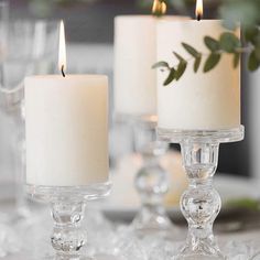 three candles sitting on top of a table next to other glass vases with flowers in them