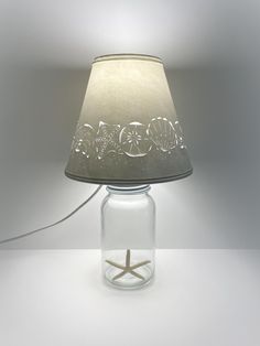 a glass lamp with a starfish in it on a white tableclothed surface