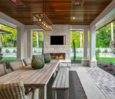 an outdoor dining area with a fireplace and television on the wall, surrounded by large windows