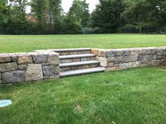 a stone wall with steps leading up to it in the middle of a grassy area