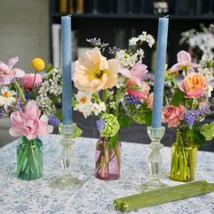 three vases with flowers and candles on a table