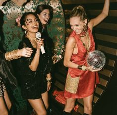 three women standing next to each other in front of a microphone and holding a disco ball