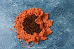 an orange and brown crocheted flower on a blue surface