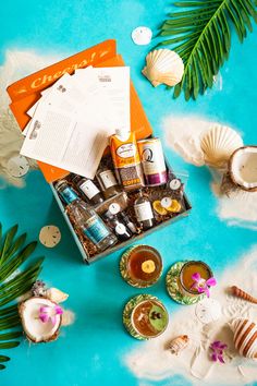 a box filled with lots of different items on top of a blue surface next to palm leaves