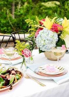 a table set with plates and flowers in vases on top of it, next to a bowl of salad