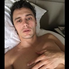 a shirtless man laying in bed with his hands on his chest and looking at the camera