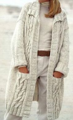 a woman standing on the beach wearing white pants and a long cardigan sweater with an open