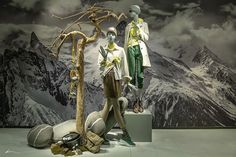 two mannequins dressed in green and white standing next to each other with mountains behind them