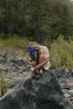 a woman sitting on top of a rock holding flowers