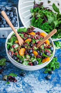 a salad with blueberries, oranges and spinach in a white bowl on a blue table