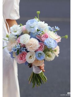 a bride holding a bouquet of white and blue flowers in her hand on the street