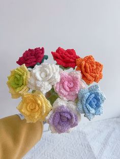 crocheted flowers are arranged in a vase on a white tablecloth with a person's hand holding the bouquet