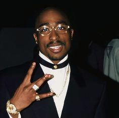 a man in a tuxedo and glasses making the peace sign with his hand