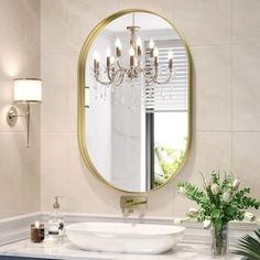 a white sink sitting under a round mirror in a bathroom next to a vase with flowers