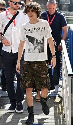 a man walking across a wooden bridge next to other men in shorts and t - shirts