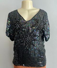 "Vintage 70s Sequins Silk Blouse by Sarafino. Made in India, this silk top features a floral aabstract design made with sequins and long beads over a black background.  CONDITION: It's missing some sequins on top of one of the shoulders which is reflected in the price. No size label. Estimated size: L Approx Flat Measurements:  Bust: 40\" Waist: 38\"  Length: 25\" Most of our pieces are pre-loved vintage or antique items. They will sometimes have some wear as they are at least 20 years old. Plea Festive V-neck Top For Party Season, Festive Silk Party Tops, Black Disco Tops For Summer, Black Disco Top For Summer, Festive Black Top For Night Out, Vintage Short Sleeve Tops For Party, Silk Party Tops With Sequins, Retro V-neck Blouse For Party, Retro Spring Party Blouse