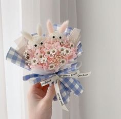 a hand holding a bouquet of flowers with bunny ears on it's head and ribbon