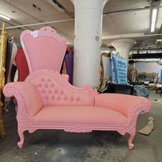 a pink couch sitting on top of a floor next to a pile of chairs in a room