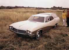 two people standing next to an old car in a field