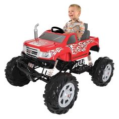 a young boy riding on the back of a red toy truck with monster wheels and tires