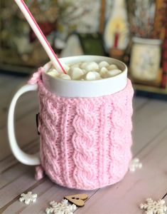 a pink knitted cup with marshmallows in it and a straw sticking out of the top