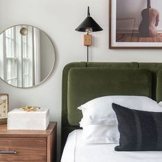 a bedroom with a green headboard and white linens on the bed next to a clock