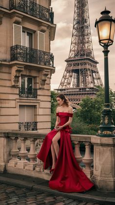 a woman in a red dress sitting on a ledge near the eiffel tower