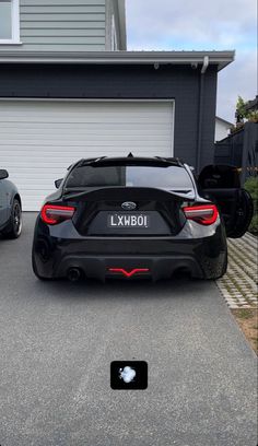 two cars parked next to each other in front of a house with garage doors open