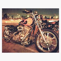 two motorcycles parked next to each other in a parking lot at night with city lights behind them