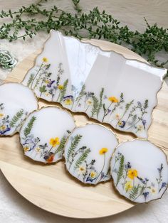 six decorated cookies on a plate with flowers and leaves around them, sitting on a table