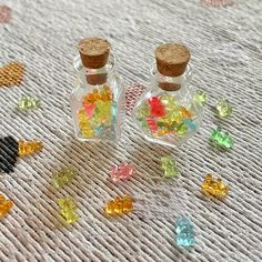 two small glass bottles filled with different colored stones on top of a white table cloth