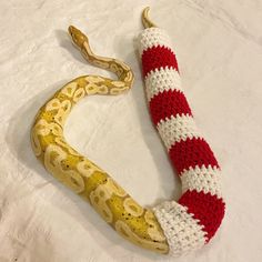 a snake wrapped in knitted fabric on top of a white bed sheet with a red and white stripe