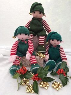 three knitted elves sitting on top of each other next to holly wreaths and bells