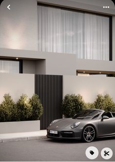 a grey sports car parked in front of a modern house with white curtains on the windows