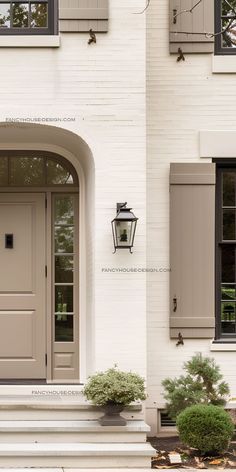 the front door to a white house with shutters and window boxes on either side