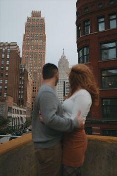 a man and woman standing next to each other in front of tall buildings on a cloudy day