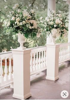 two white vases with flowers are sitting on the porch railing next to each other