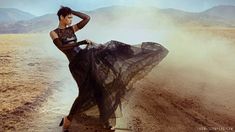 a woman in black dress standing on dirt road