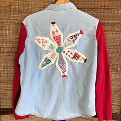 a blue jean jacket with an embroidered flower on the front and red sleeves, hanging from a wooden hanger