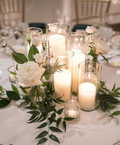 a table topped with lots of white candles and flowers next to glasses filled with water