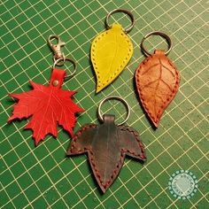 three leather leaf shaped key chains sitting on top of a green table next to each other