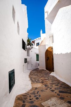 an alley way with white walls and cobblestone flooring in front of a wooden door