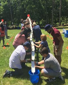 several people are gathered around a water pipe in the grass with orange cones on it