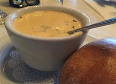 a bowl of soup next to a roll on a plate