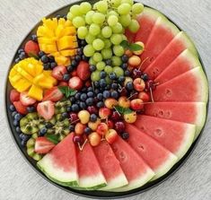 a plate filled with watermelon, grapes, and other fruits