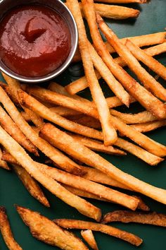 french fries and ketchup on a green plate next to a bowl of ketchup