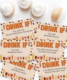 four drink if cards sitting on top of a table next to cupcakes