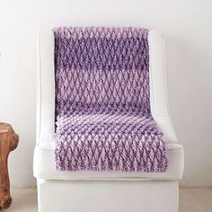 a purple knitted blanket sitting on top of a white chair next to a wooden table