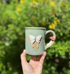 a hand holding a coffee cup with a butterfly painted on it