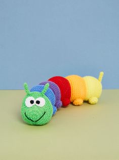 a crocheted caterpillar is sitting on a table with a blue wall in the background